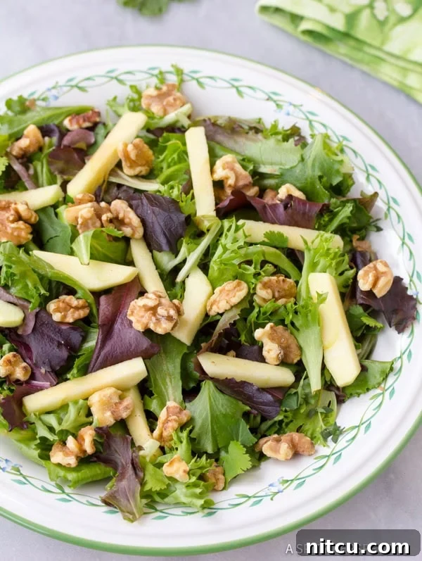 Bowl with fresh greens topped with diced apples and toasted walnuts, ready for dressing.