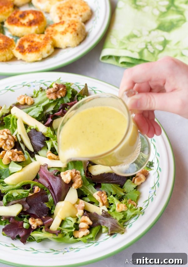 A hand drizzling homemade vinaigrette dressing over a prepared salad.