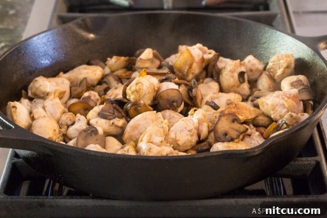 Cooked mushrooms and chicken browning in a skillet.