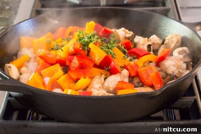Chopped bell peppers added to the chicken and mushroom mixture in a skillet.
