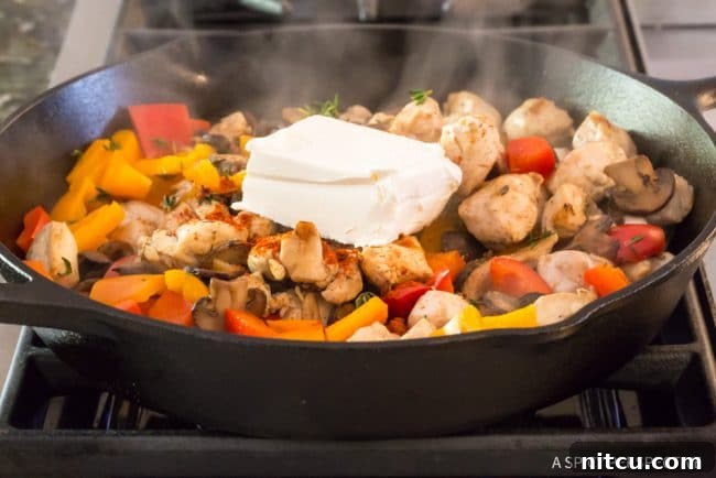 Chicken and vegetables topped with dollops of cream cheese in a skillet, ready to melt into sauce.