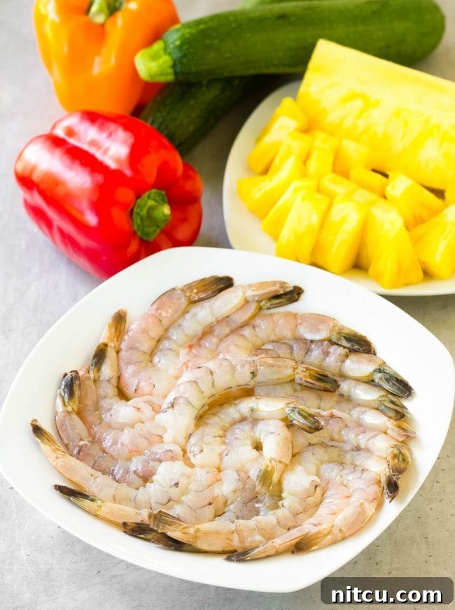 Overhead view of raw shrimp in a bowl, surrounded by fresh ingredients for the skewers.