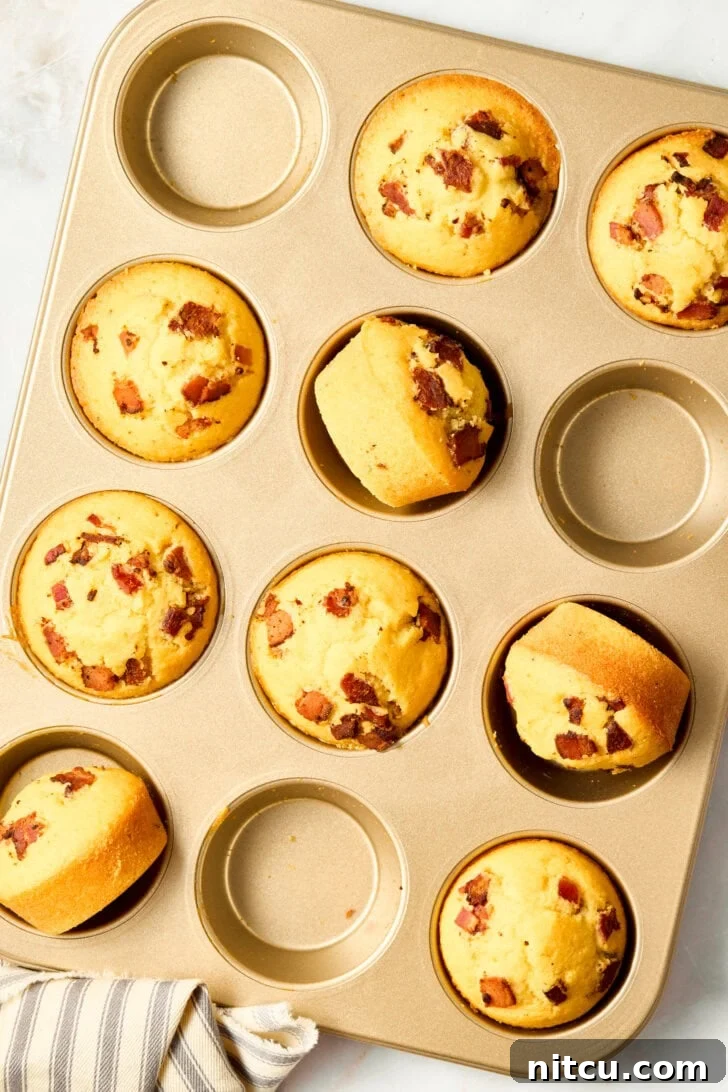 Warm cornbread muffins in a pan, garnished with bacon and maple syrup