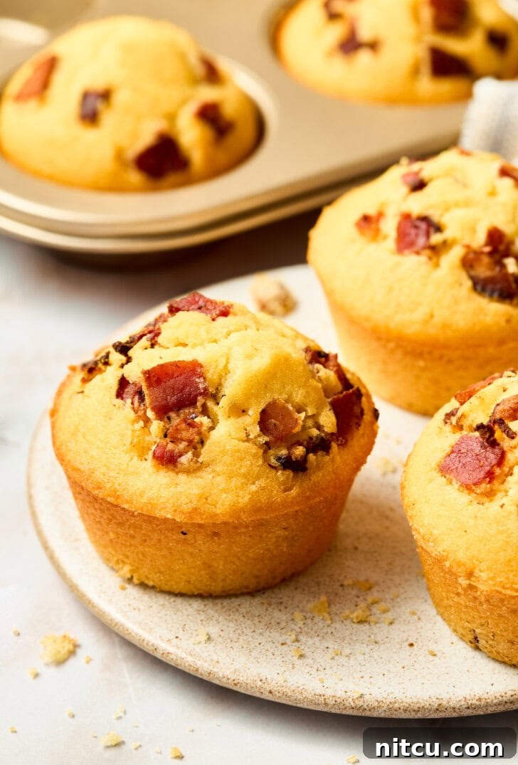 Plated warm cornbread muffins with maple syrup and bacon on top