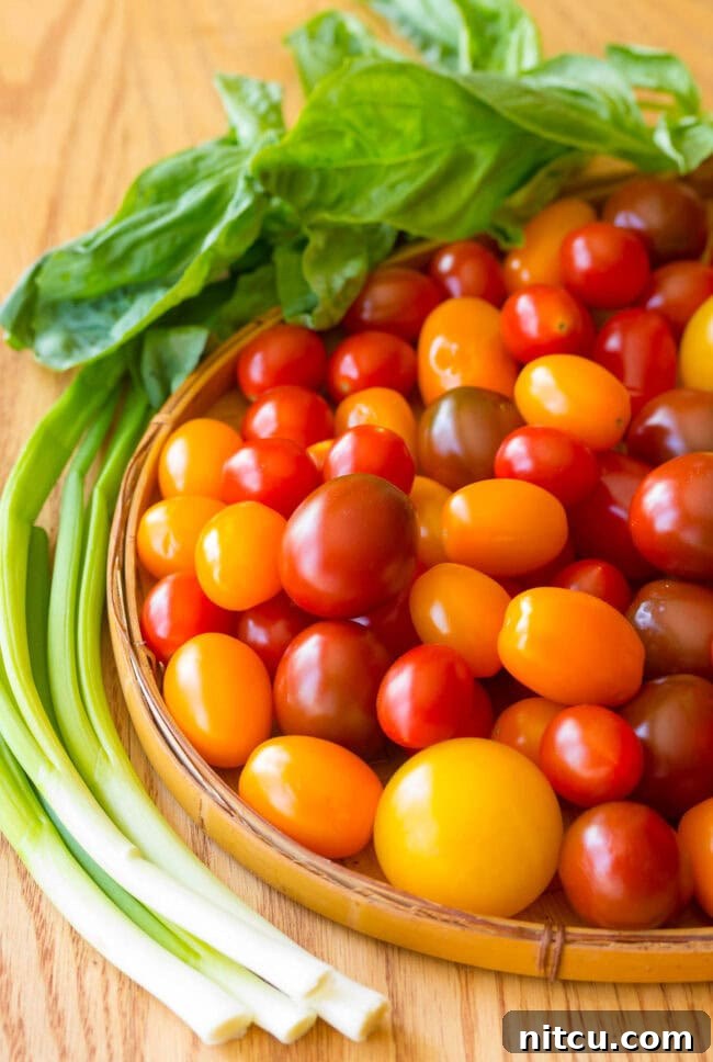 A selection of fresh produce, including bright red grape tomatoes, green onions, and basil leaves, ready for the tomato tart recipe.