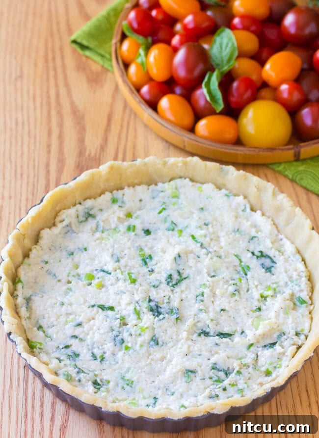 The tart crust is being pressed into a tart pan, showing the detailed crimped edges.