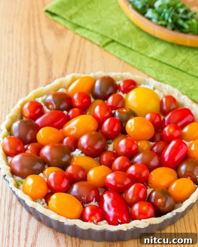 The savory cheese and herb filling is spread evenly into the tart crust before adding tomatoes.