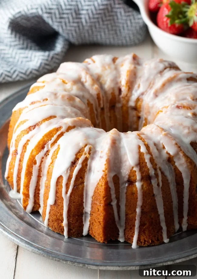 A fully prepared and beautifully glazed strawberry bundt cake, garnished with fresh berries, sitting on a silver serving plate, inviting guests to indulge.