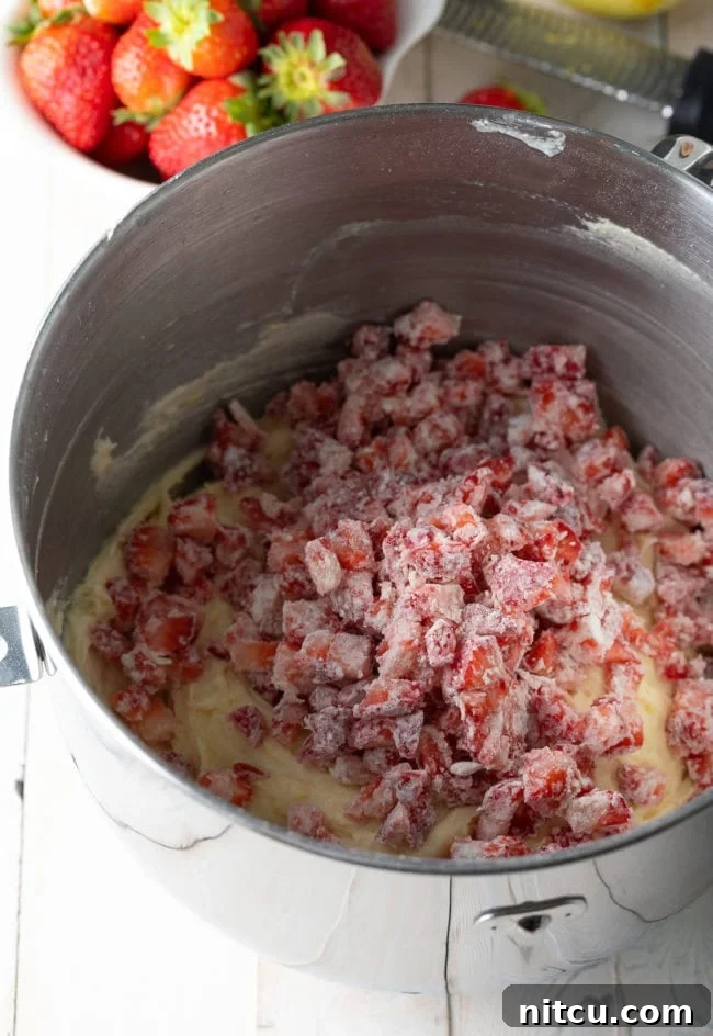 Strawberry bundt cake batter in a mixing bowl with fresh chopped strawberries placed on top, ready to be folded in.