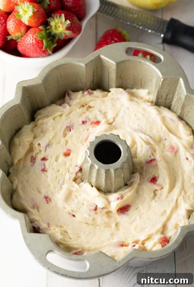 Strawberry cake batter evenly poured into a silver bundt pan, ready for baking.