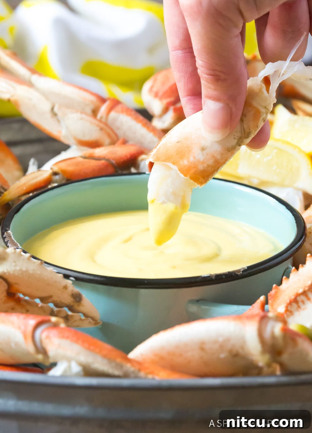 A hand gently dipping a piece of crab meat into a small bowl of the creamy, spicy mustard sauce, capturing the perfect bite.