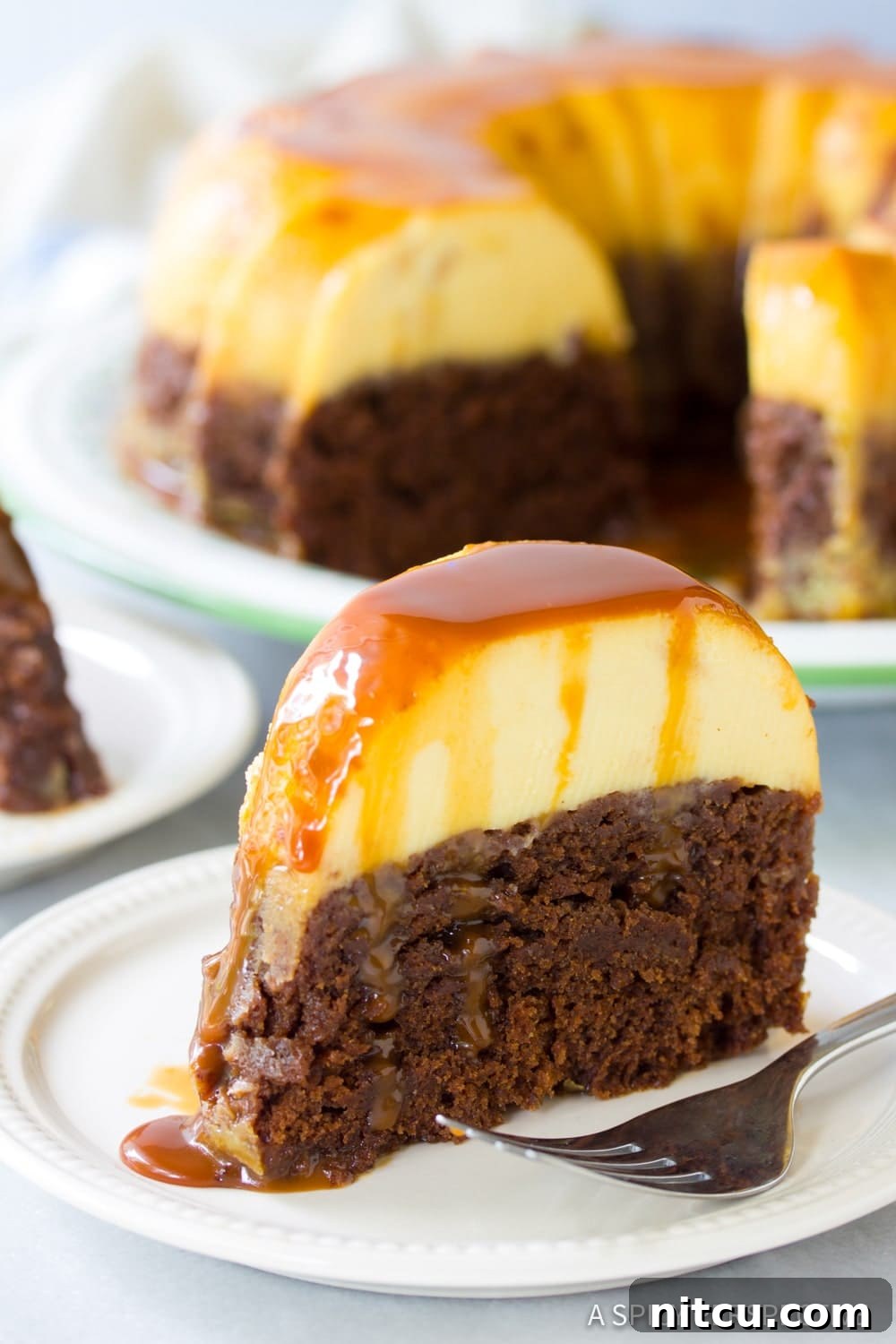 A perfectly sliced piece of Chocoflan cake revealing distinct chocolate cake and flan layers, served on a pristine white plate with a fork.