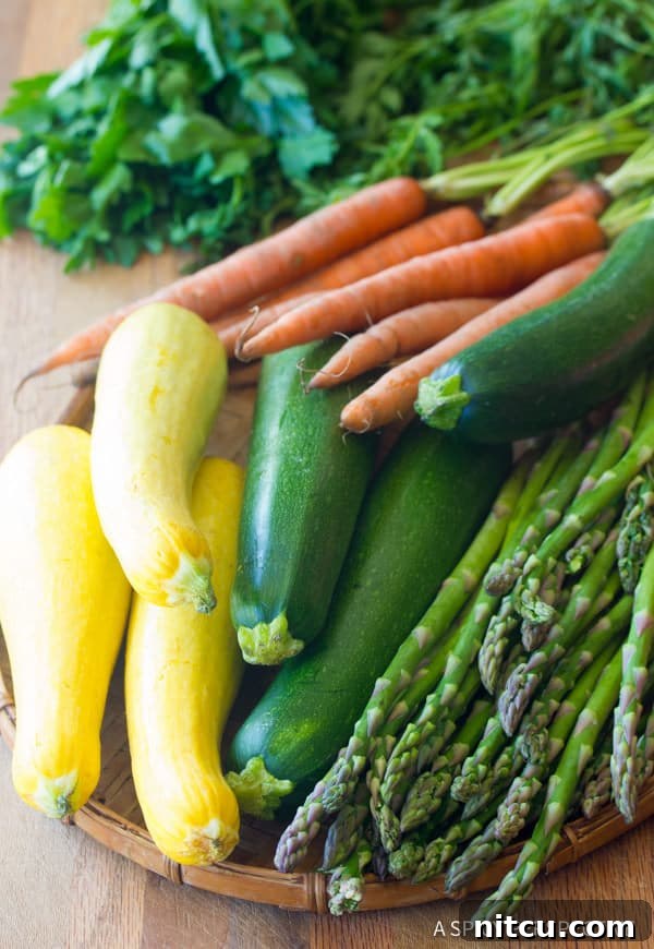 Assortment of fresh, colorful vegetables ready for roasting, including vibrant green zucchini, yellow summer squash, crisp asparagus spears, and sweet orange carrots.