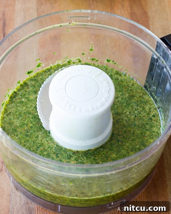 Fresh chimichurri sauce being prepared in a food processor, showing a vibrant green mixture of fresh herbs, garlic, and olive oil actively blending.