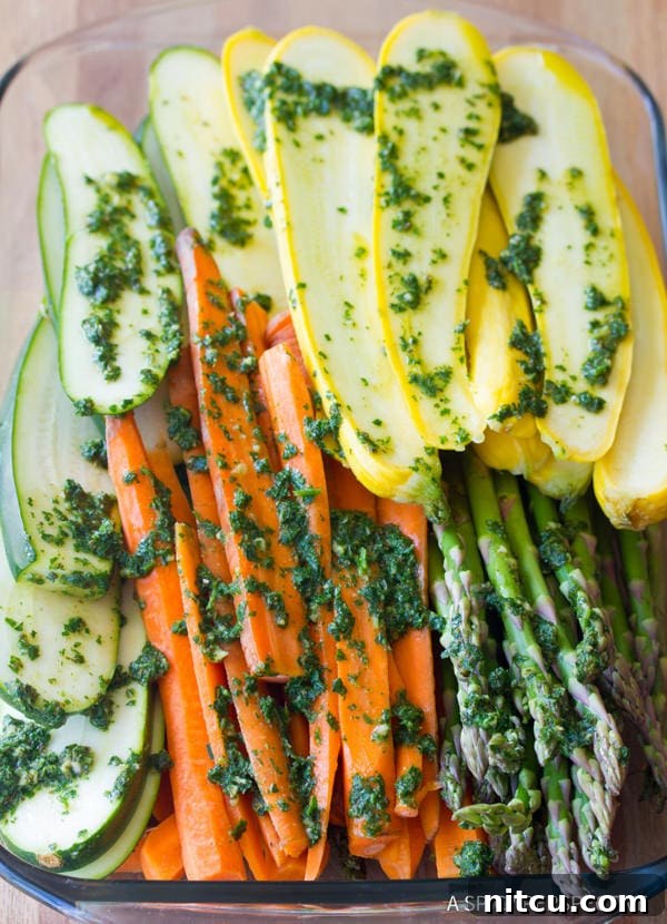 Sliced vegetables like zucchini and summer squash tossed with vibrant green chimichurri sauce in a bowl, ready for grilling or roasting.