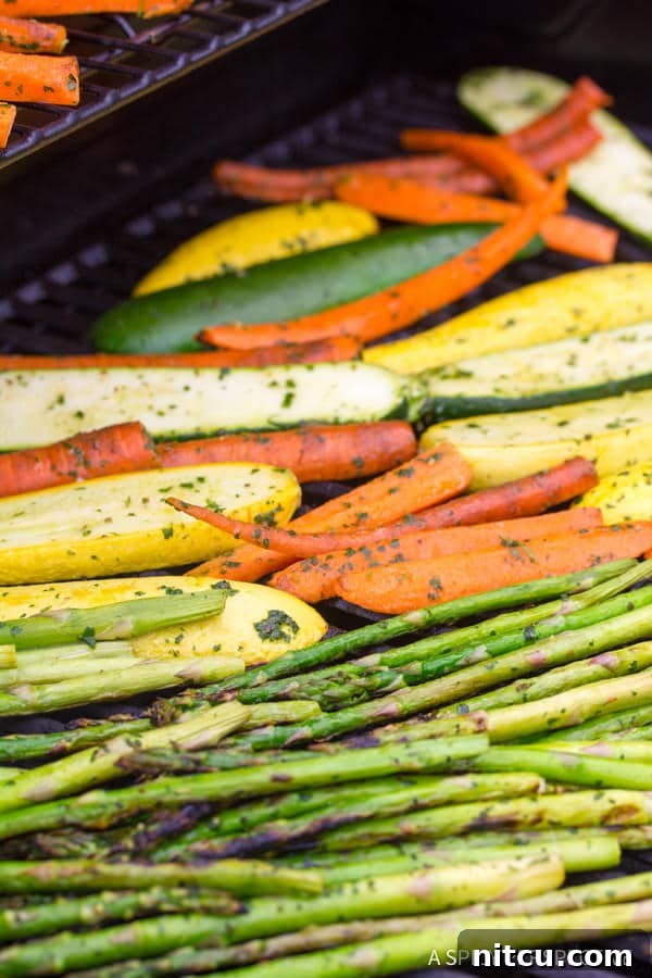 Assorted vegetables including zucchini, squash, and carrots roasting on a hot grill, showing developing char marks and vibrant colors against the grill grates.
