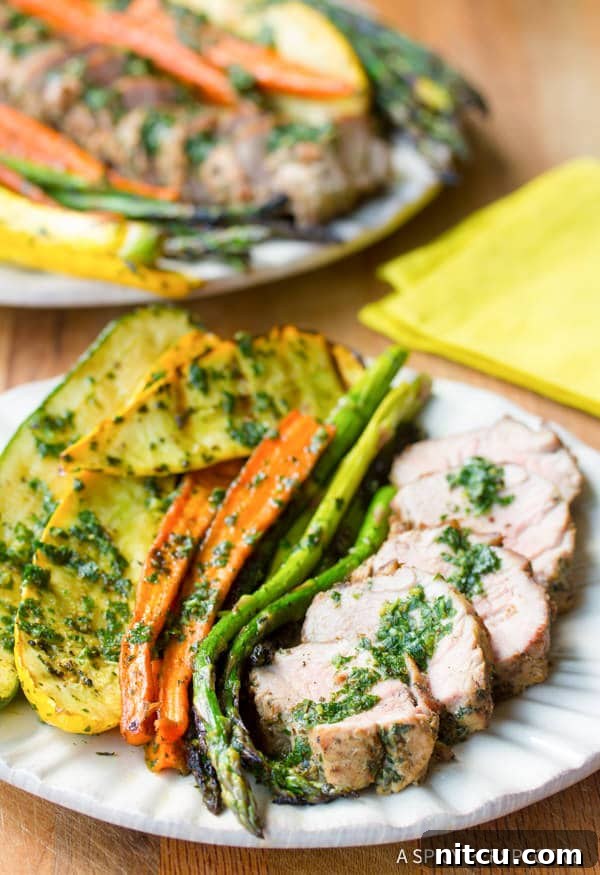 A beautifully plated single serving of grilled pork tenderloin with a side of roasted vegetables and a generous dollop of chimichurri sauce, on a rustic plate.