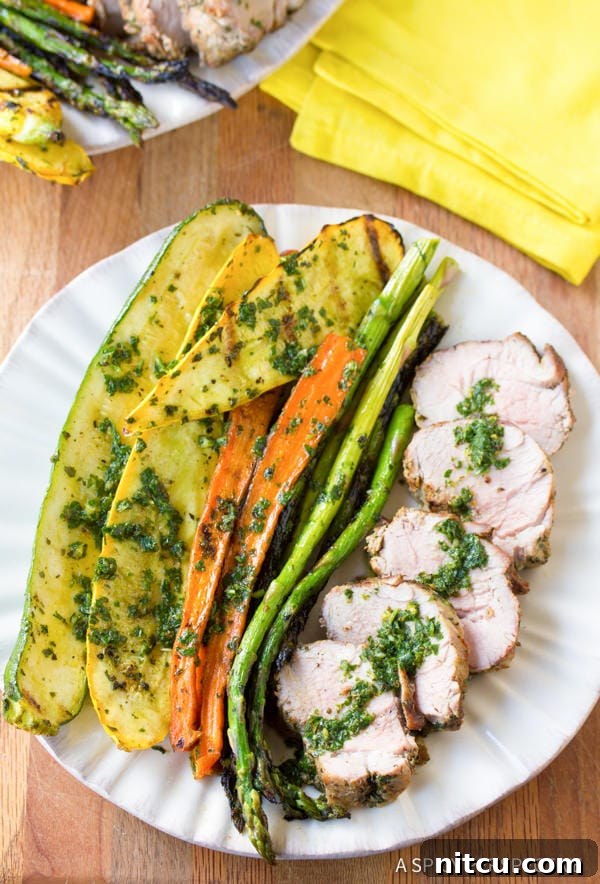 A close-up of perfectly grilled pork tenderloin slices, generously topped with fresh, vibrant green chimichurri sauce on a white plate, ready to be enjoyed.
