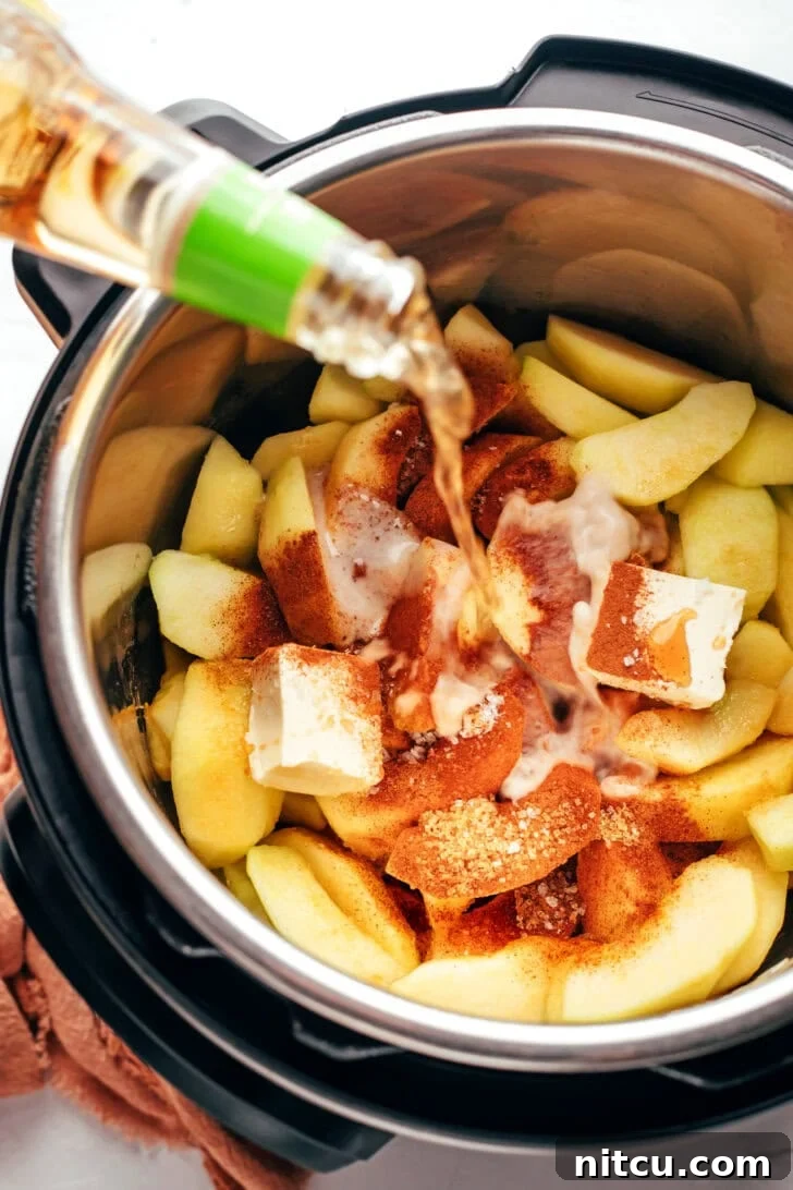 Ingredients for spiced apples in a pressure cooker while cider is being poured into the mix. 