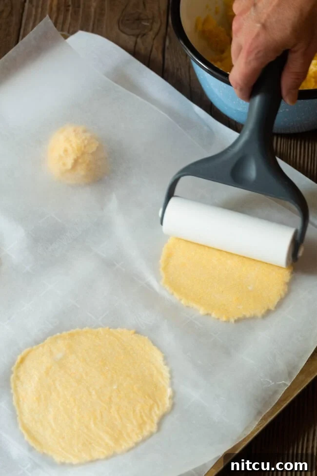Tortilla dough portions being rolled out on a parchment-lined baking sheet.