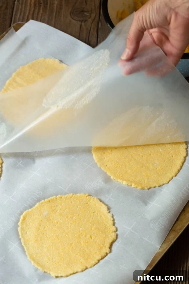 Hand pulling back the top layer of parchment to reveal perfectly flat, baked tortillas.