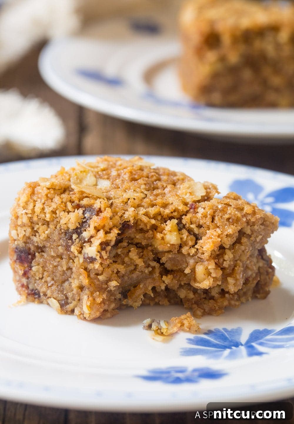 A close-up shot of a healthy egg-free oatmeal bar on a plate with a bite taken out, showing the oat, date, and nut texture.