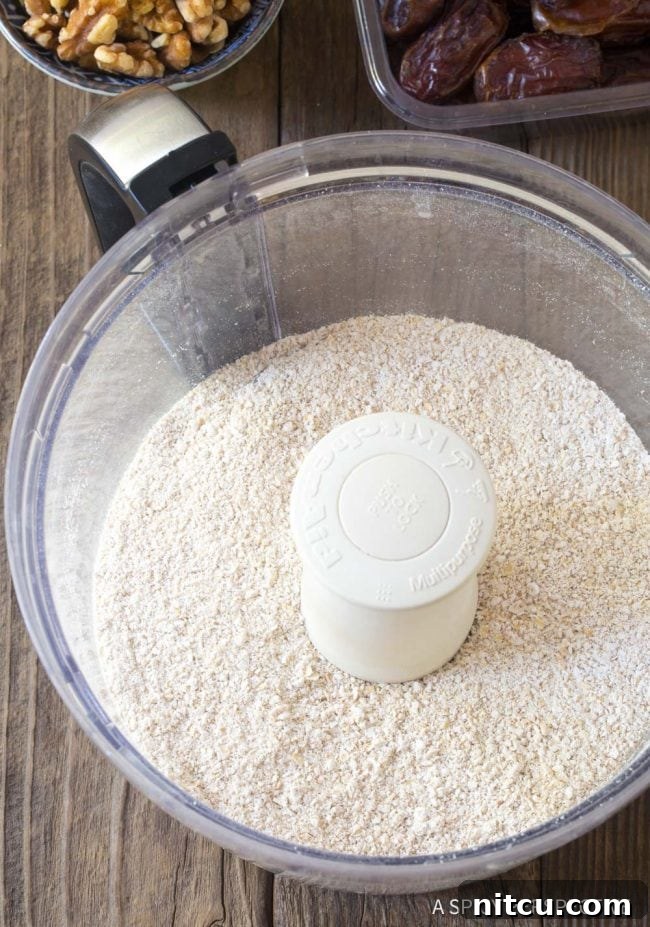 Dry oat breakfast bar ingredients, including ground flax seeds and oat flour, ready in a food processor.