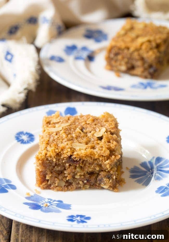 A single slice of egg-free breakfast oatmeal bar on a plate, showcasing visible nuts and dates.