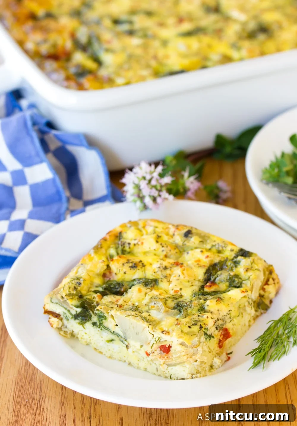 A close up photo of a slice of Greek omelette casserole on a white plate, showcasing its vibrant ingredients and fluffy texture.