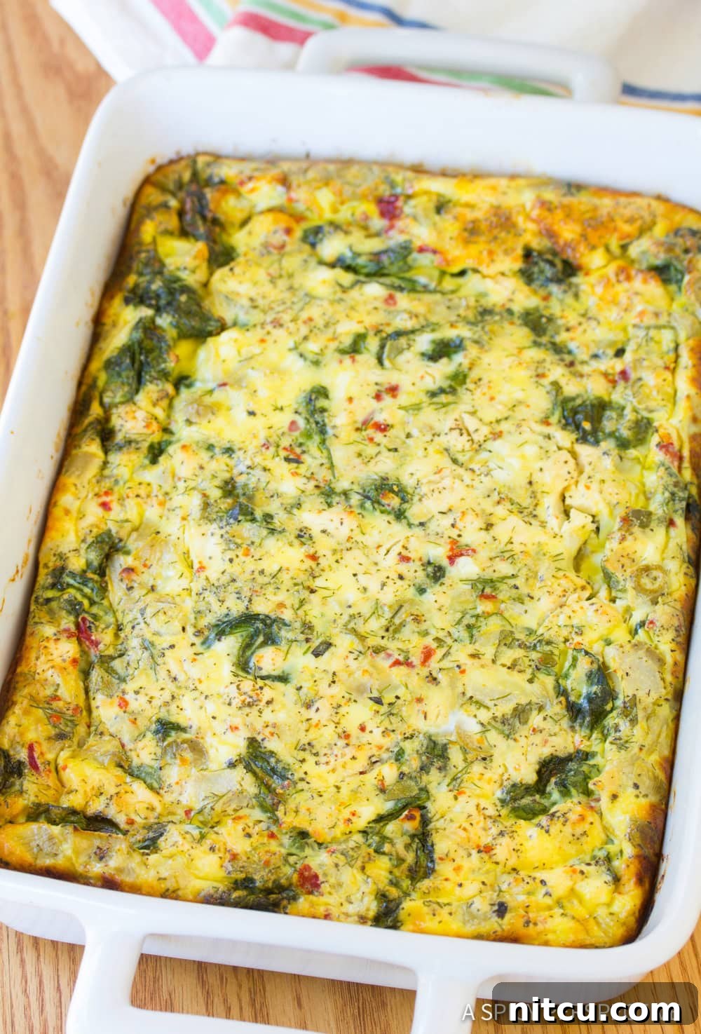 A close up view of a golden-brown Greek omelette casserole in a white baking dish, ready to be portioned and served.