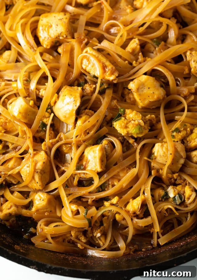 Close-up, top-down view of authentic Pad Thai chicken with noodles in a cast iron skillet, highlighting the rich texture and garnishes.
