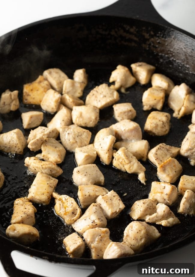 Bite-sized chicken pieces sizzling and cooking in a large, hot skillet, forming the base of the stir-fry.