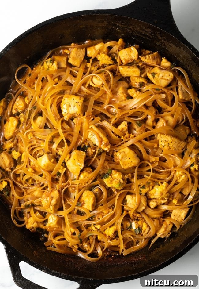Top-down view of authentic Pad Thai chicken with noodles, served hot in a cast iron skillet.