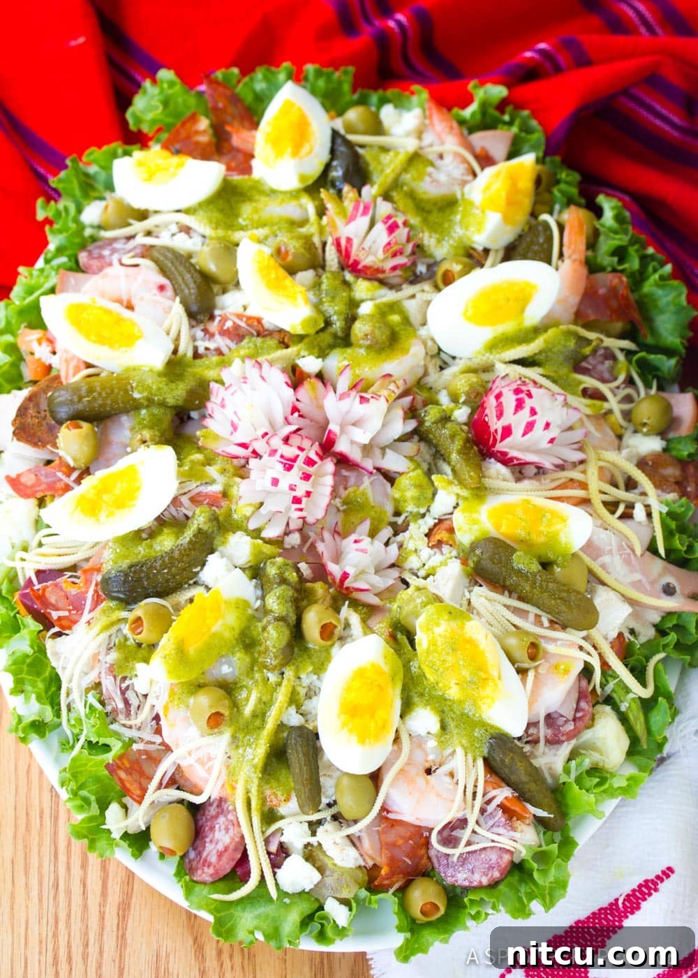 Large, colorful Fiambre salad on a serving platter with a vibrant red cloth underneath, showcasing its diverse ingredients.