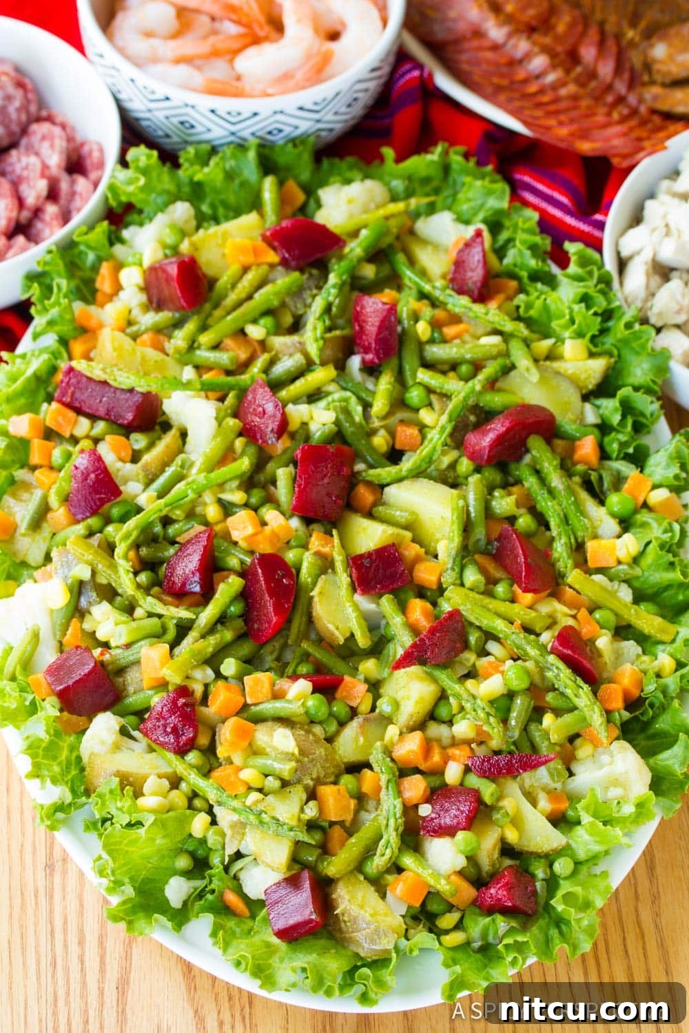 A large serving platter piled high with vibrant Guatemalan Fiambre salad, surrounded by various individual ingredients in bowls.