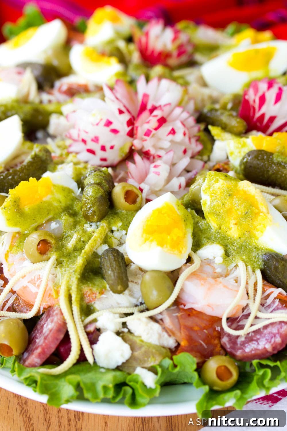 A close-up of Fiambre salad featuring lettuce, an assortment of cured meats, olives, pickles, hard-boiled eggs, and decorative radishes.