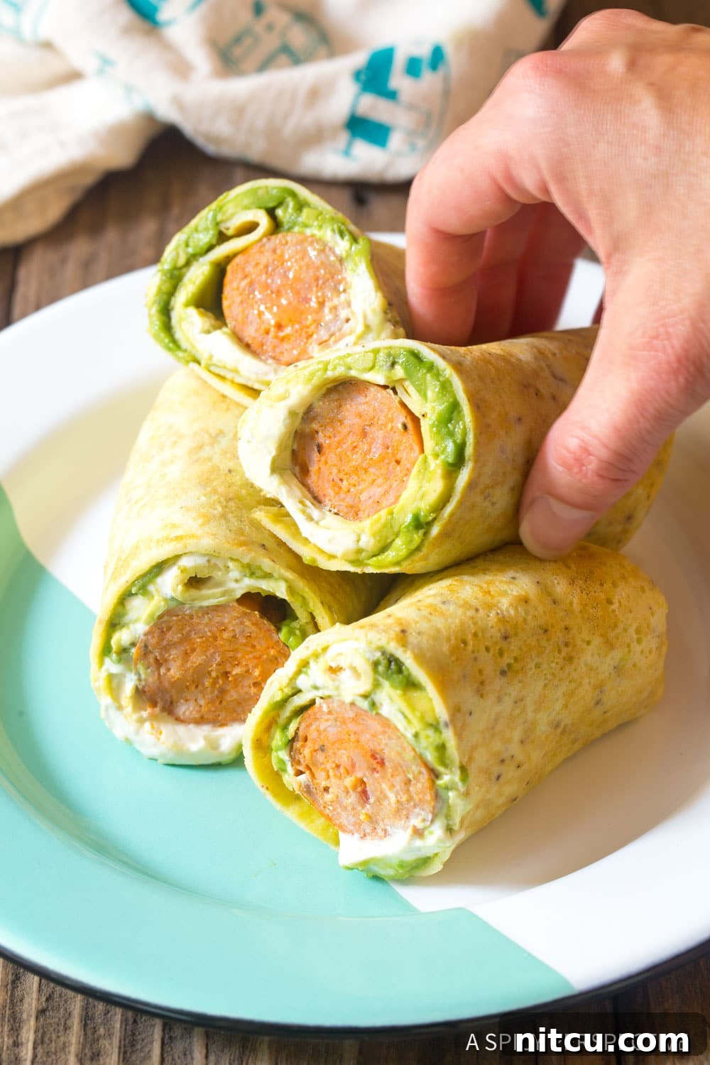 Breakfast egg wraps on a plate with a hand grabbing one. 