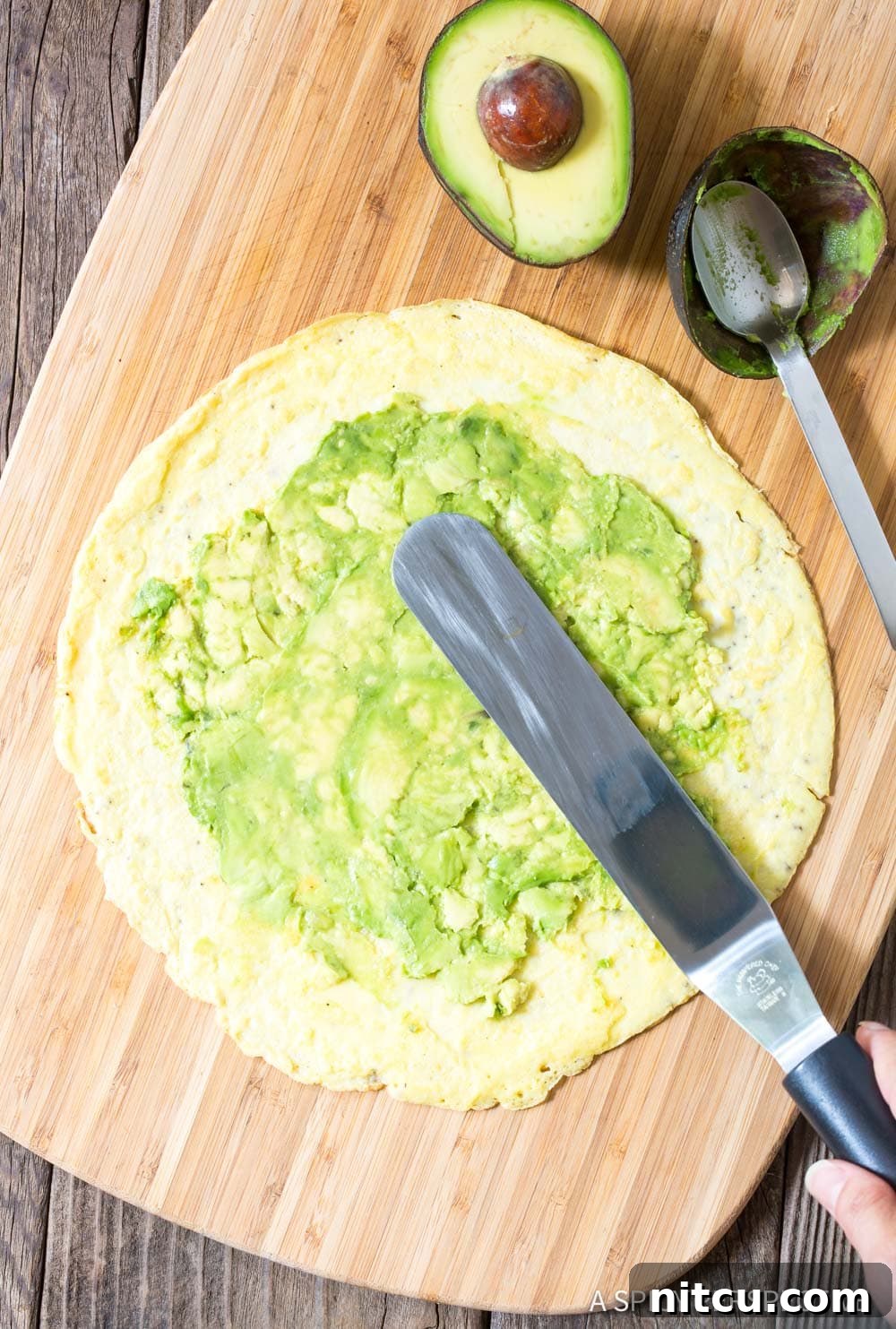 Hand spreading smashed avocado over an egg wrap. 
