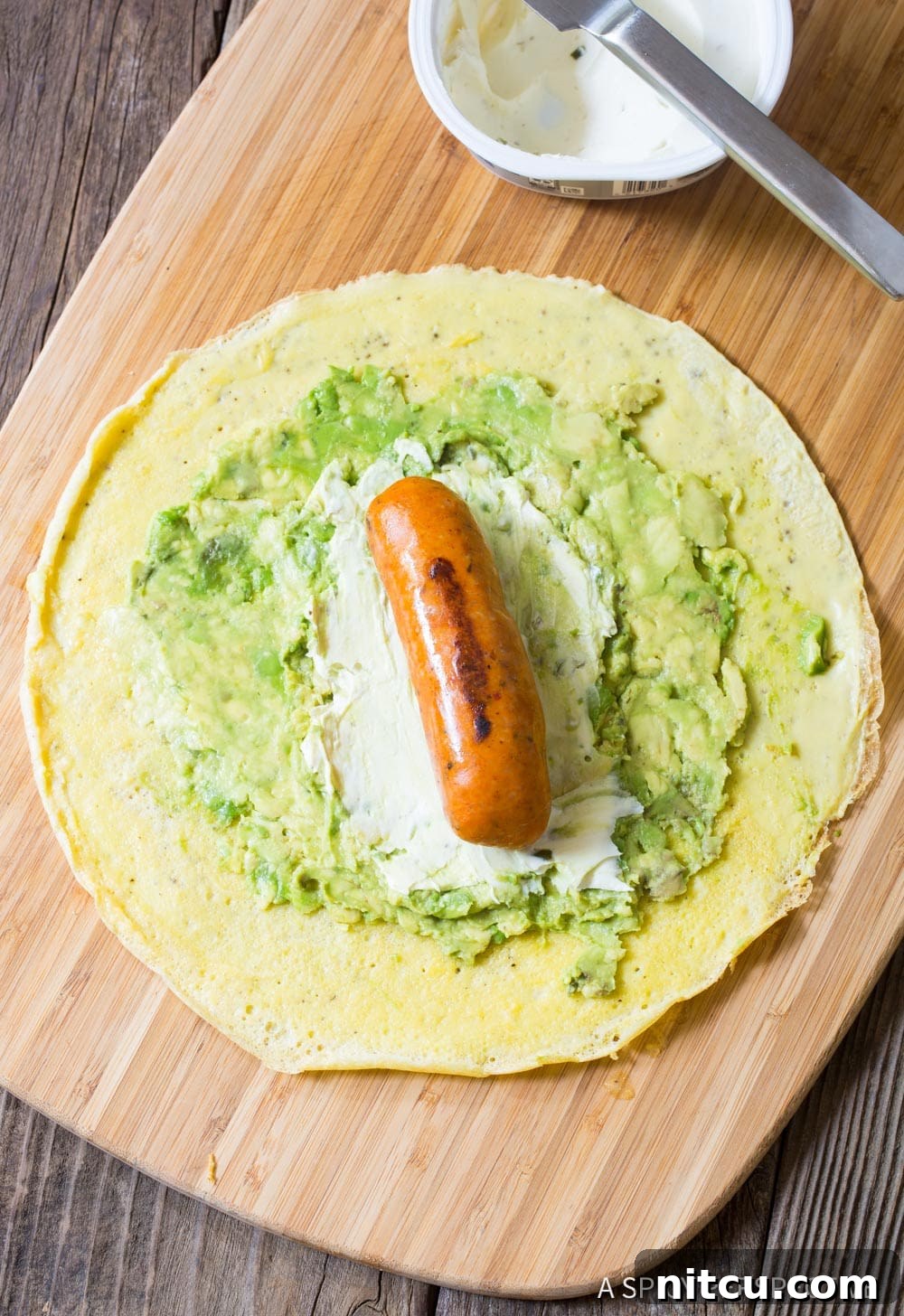 Assembling the keto breakfast egg wraps on a wooden cutting board. 