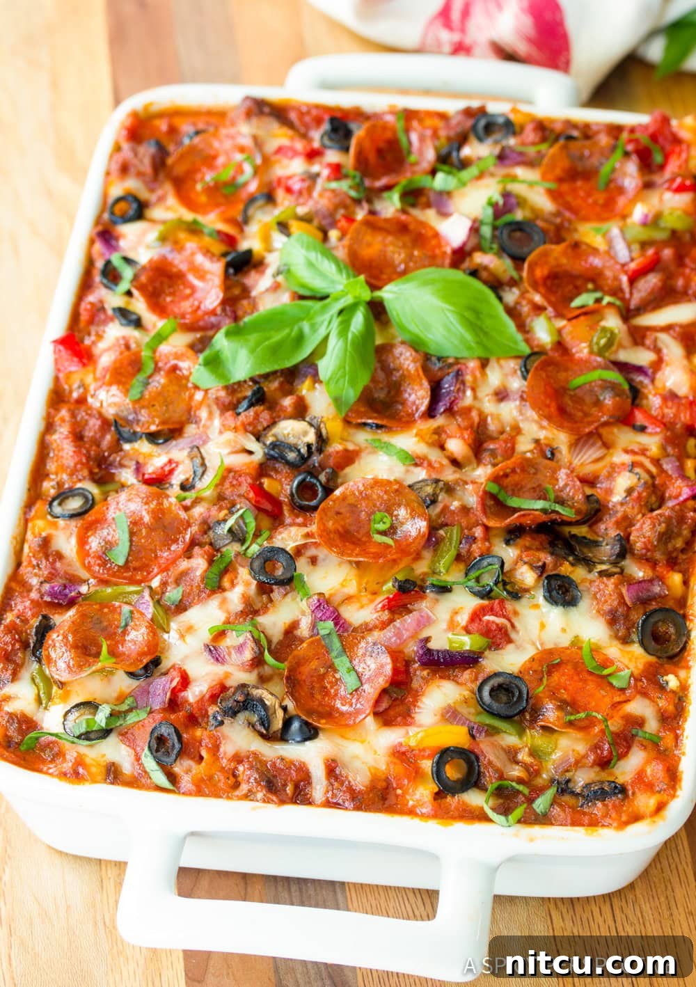 A beautifully baked Supreme Pizza Lasagna, topped with fresh basil leaves, ready to be served from a white baking dish.