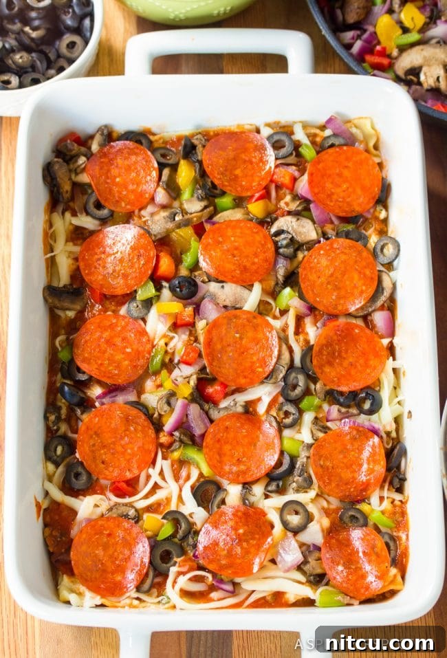 A second overhead view of the Supreme Pizza Lasagna mid-layering in a white pan, showcasing the vibrant ingredients and building structure before baking.