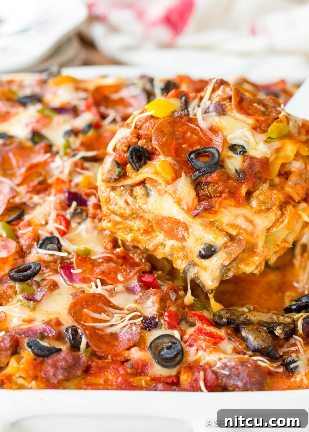 A knife gently slicing into a pan of freshly baked Supreme Pizza Lasagna, revealing the luscious, cheesy layers within.