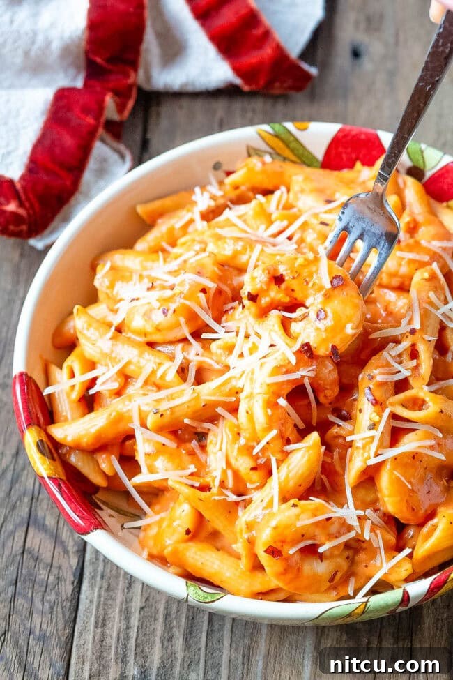 Bowl of penne alla vodka with shrimp with a fork taking a piece of shrimp. I