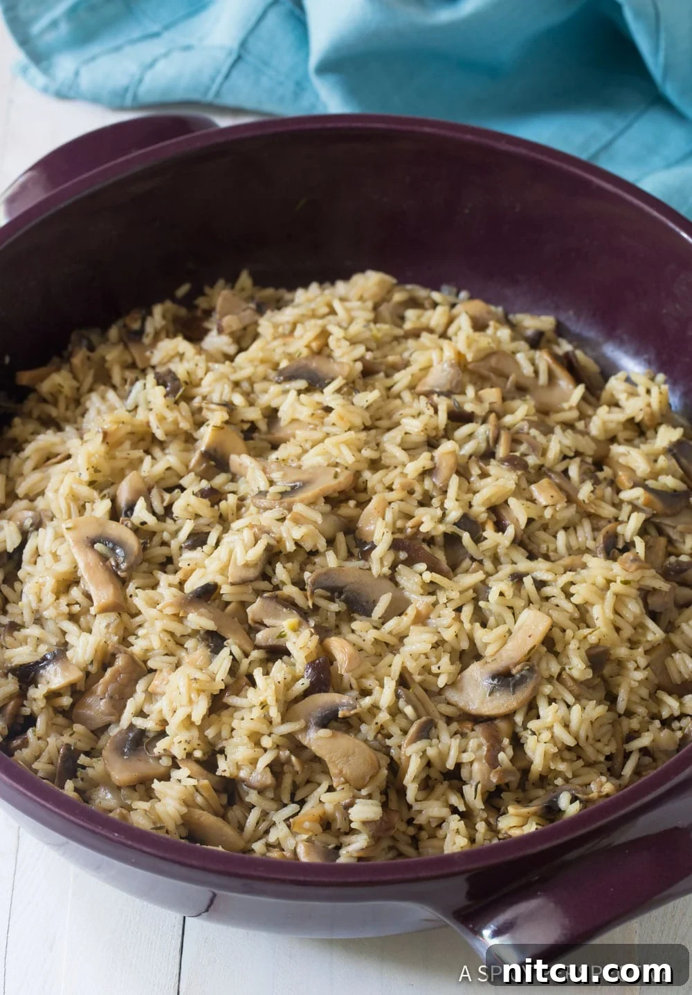 A wide shot of cooked mushroom rice pilaf in a large pan, showcasing its fluffy texture and rich, golden-brown mushrooms.