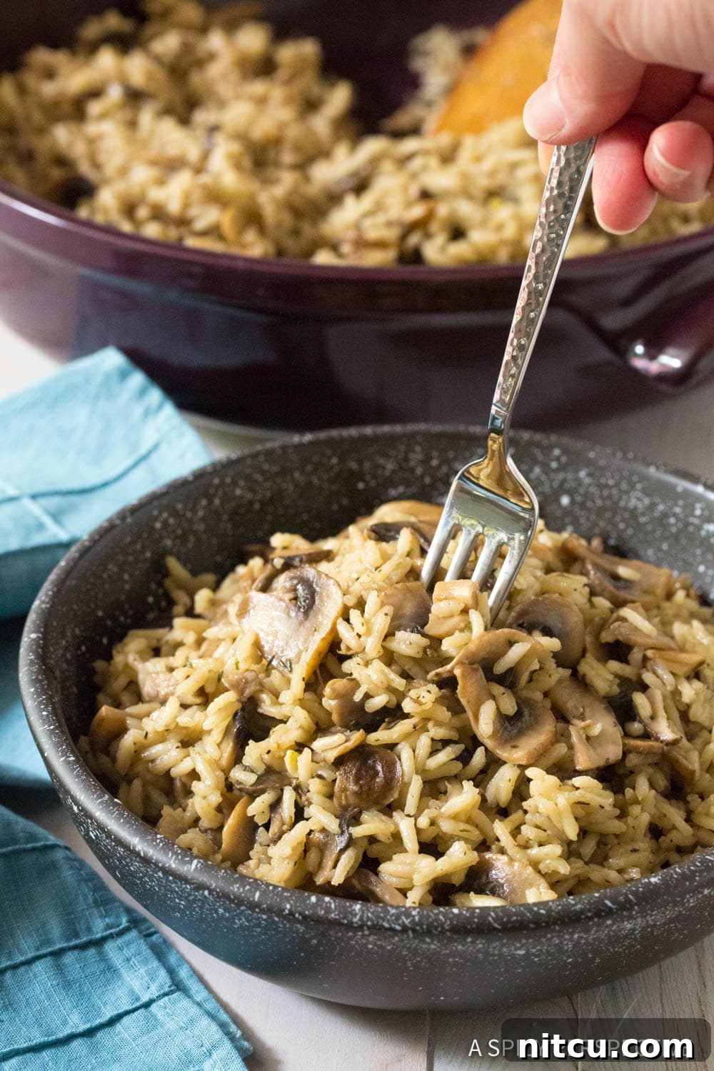 A hand gently putting a fork into a black bowl filled with savory mushroom rice pilaf, highlighting its fluffy texture.