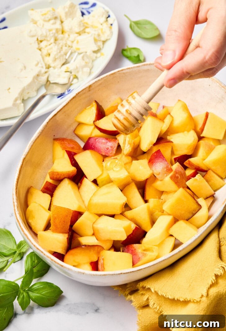 Close-up of chopped peach salad ingredients in a mixing bowl, showcasing vibrant peaches and fresh basil.