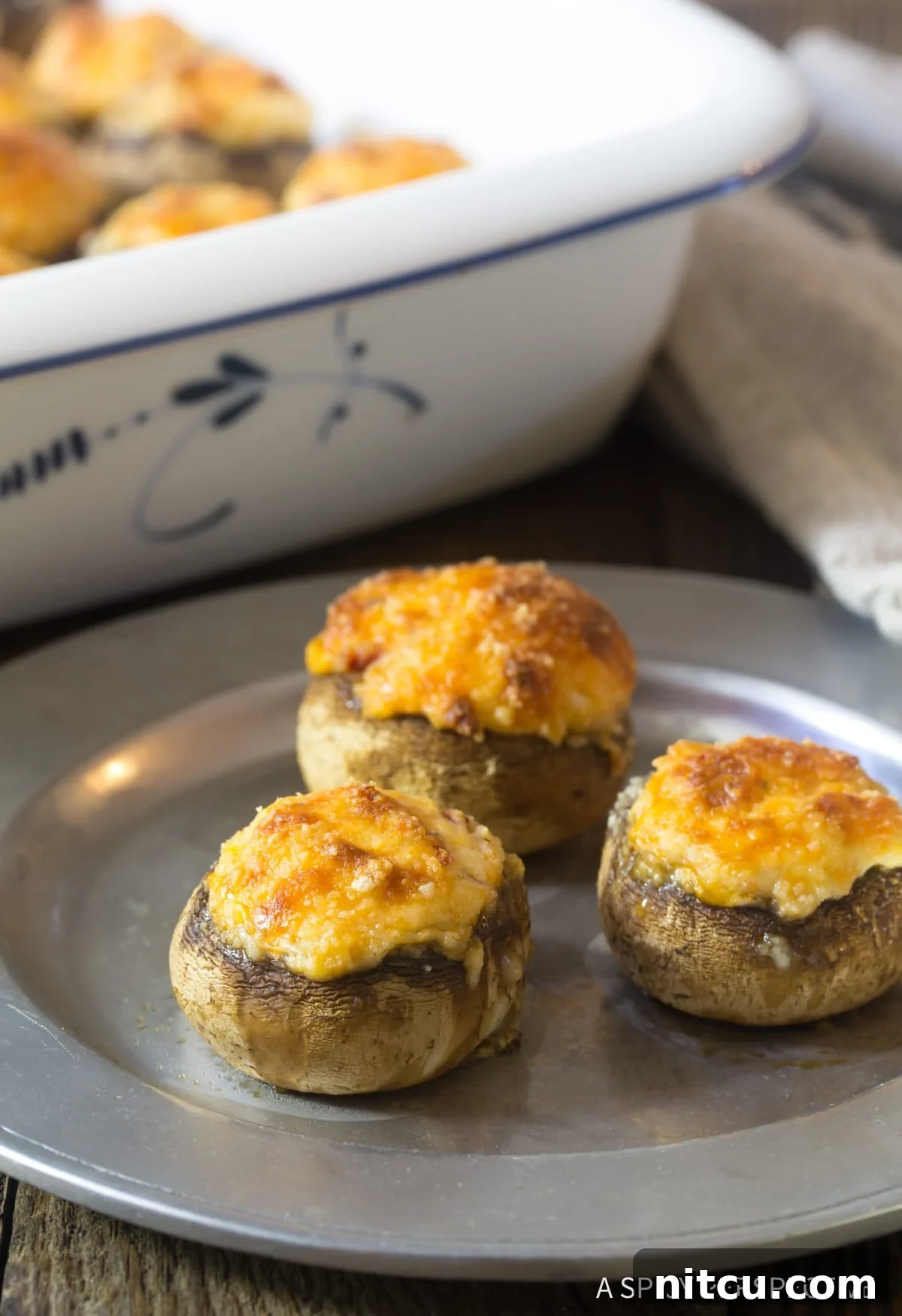 A plate featuring several perfectly cooked cheese stuffed mushrooms, enticingly ready to be picked up and enjoyed as a snack.