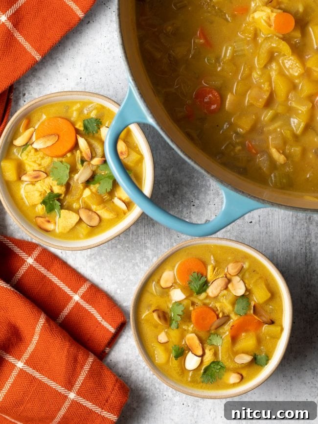 An overhead shot of a pot of Mulligatawny soup and two individual bowls garnished with sliced almonds.