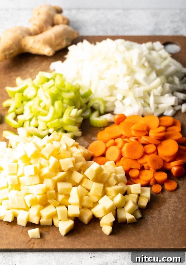 A cutting board laden with freshly chopped ingredients including onions, celery, carrots, and apples, ready for Mulligatawny soup preparation.