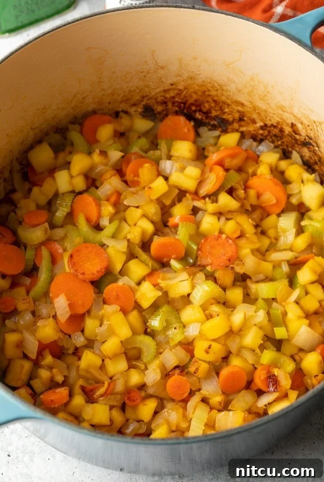 A close-up view of a pot on the stove, showing onions, vegetables, and apples browning and sautéing, releasing their aromatic flavors.
